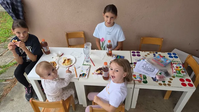 Djeca jedu i crtaju za dječjim stolom
