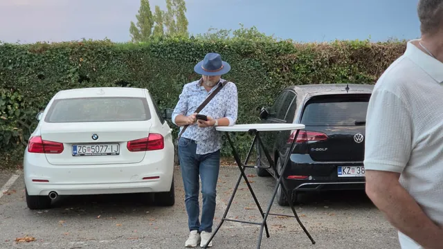 Gost sa šeširom uz visoki stol na parkiralištu