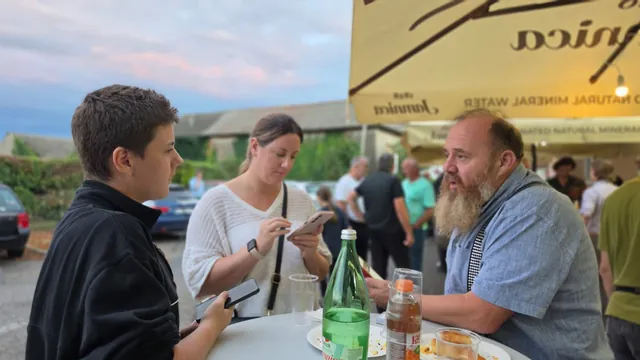 Gosti razgovaraju za stolom pod suncobranom ispred doma