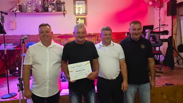 Dobitnik ponosno drži diplomu uz domaćine na pozornici