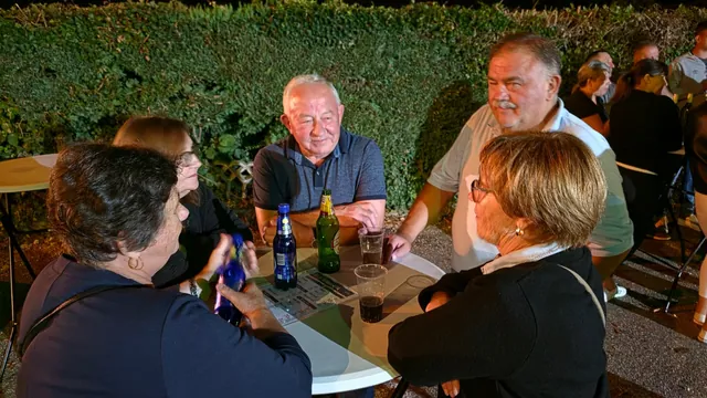 Društvo uz stajaći stol pored živice u noćnim satima