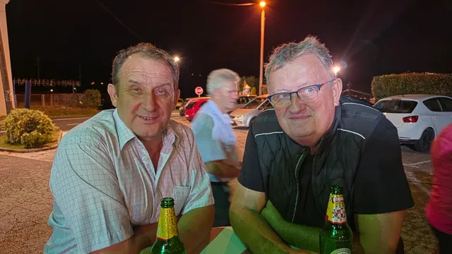 Dva gosta uz pivo za stolom ispred doma navečer