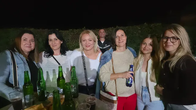 Skupina posjetiteljica pozira uz stol pun pića navečer