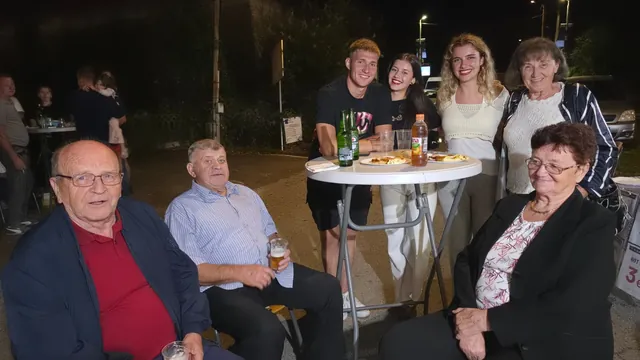 Mladi i stariji gosti oko stajaćeg stola navečer