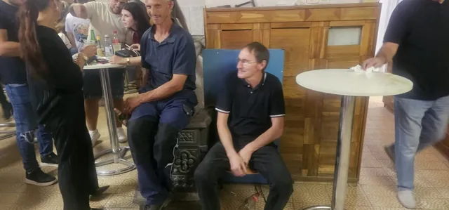 Dvojica muškaraca sjede i razgovaraju kraj stare peći